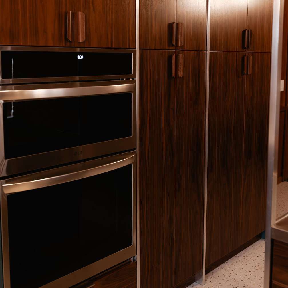 A built-in stainless steel double oven set into dark, vertically grained wood cabinetry in a modern kitchen.