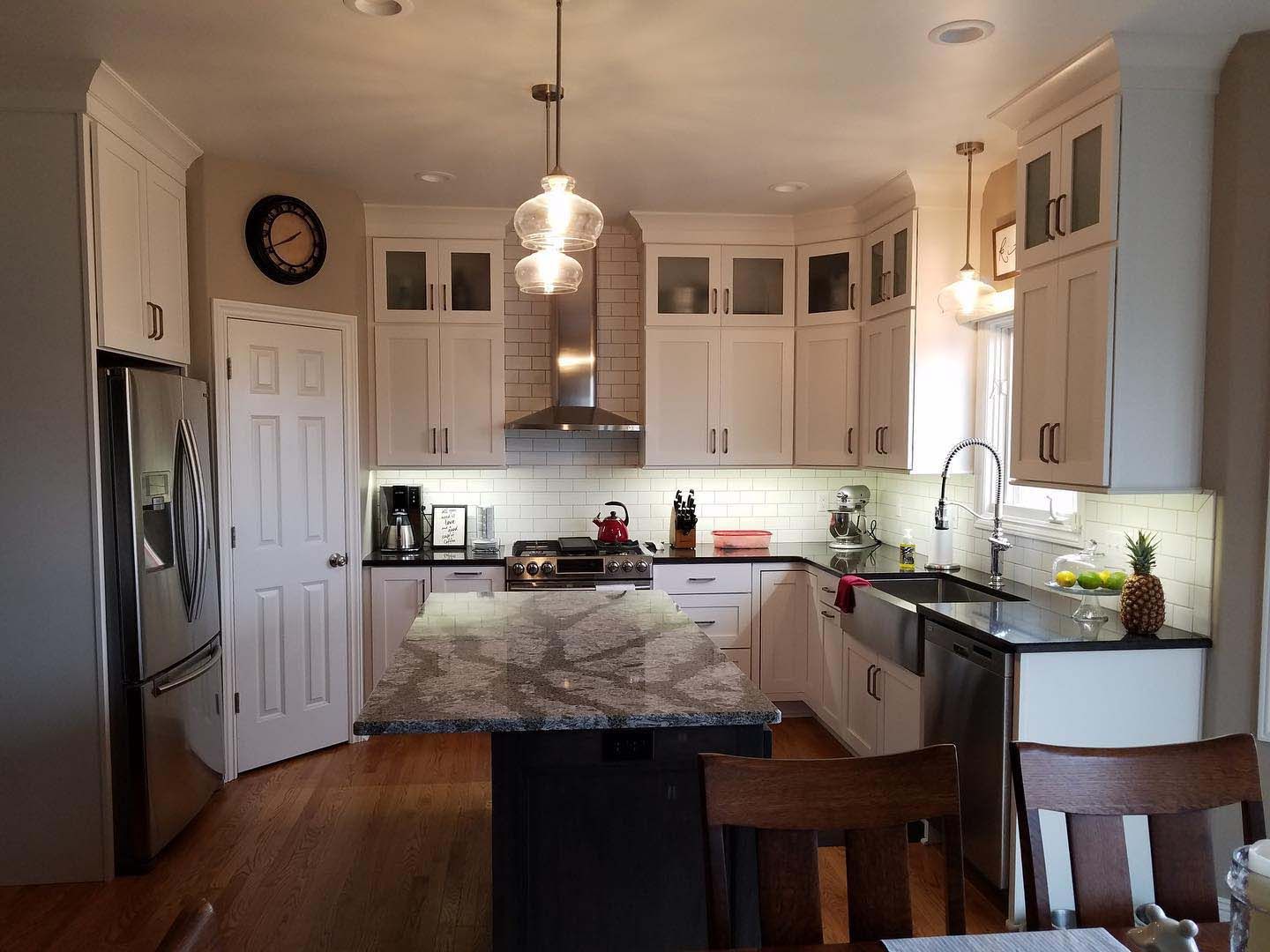 A well-lit kitchen features white cabinets, a black granite island, stainless steel appliances, and wood floors.
