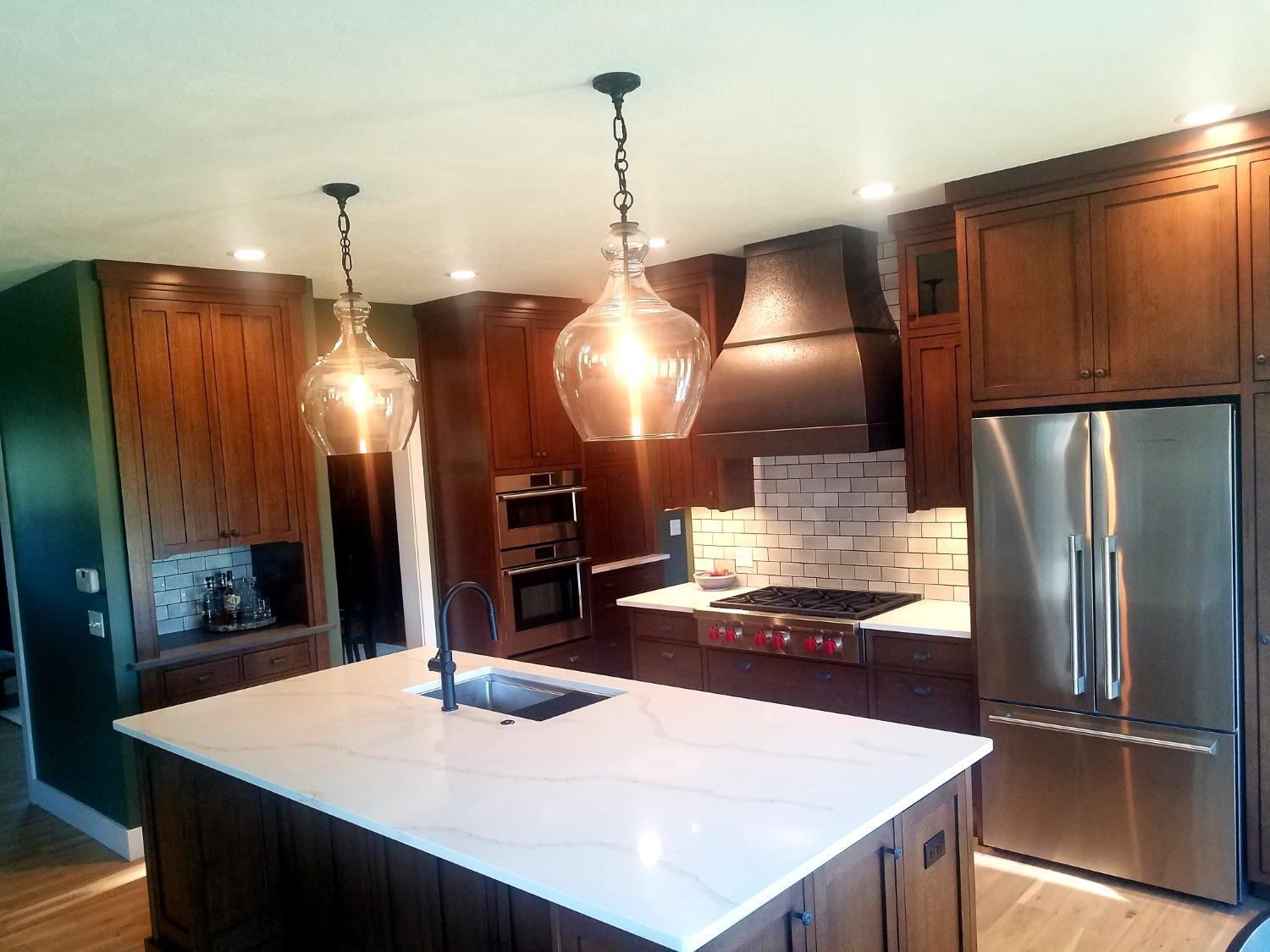 A kitchen with dark wood cabinets, a large white quartz island, stainless steel appliances, and two pendant lights.