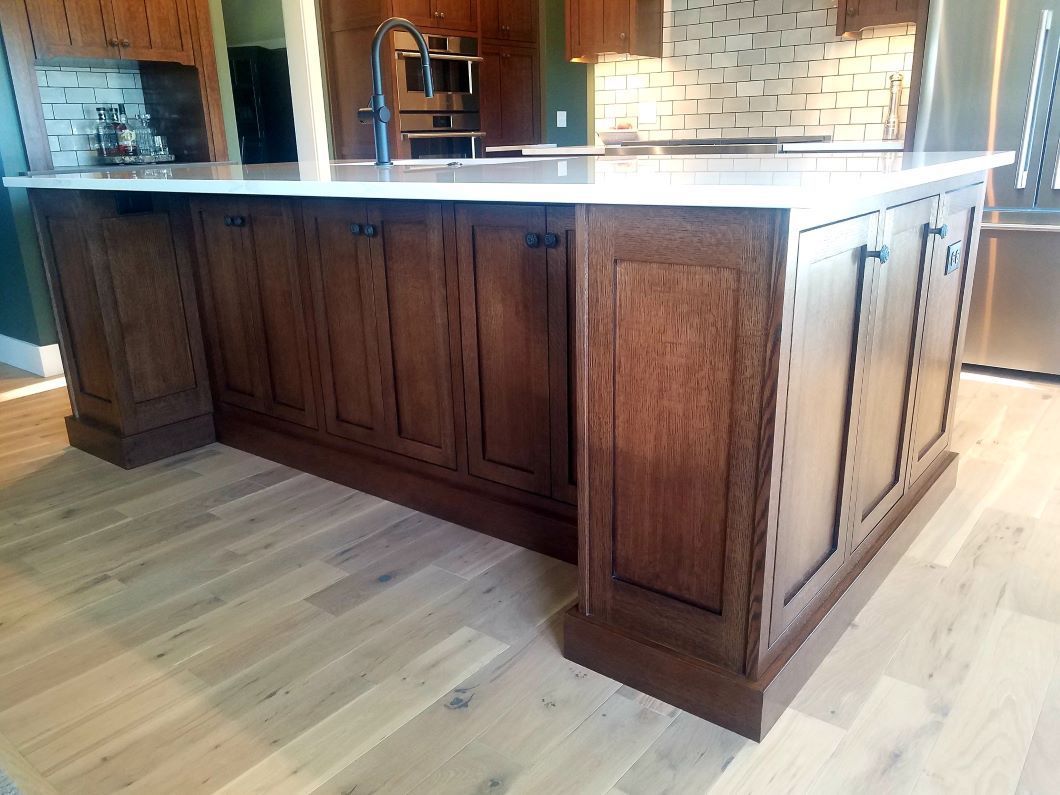 A dark wood kitchen island with a white countertop, featuring paneled cabinet doors, set on light wood flooring.