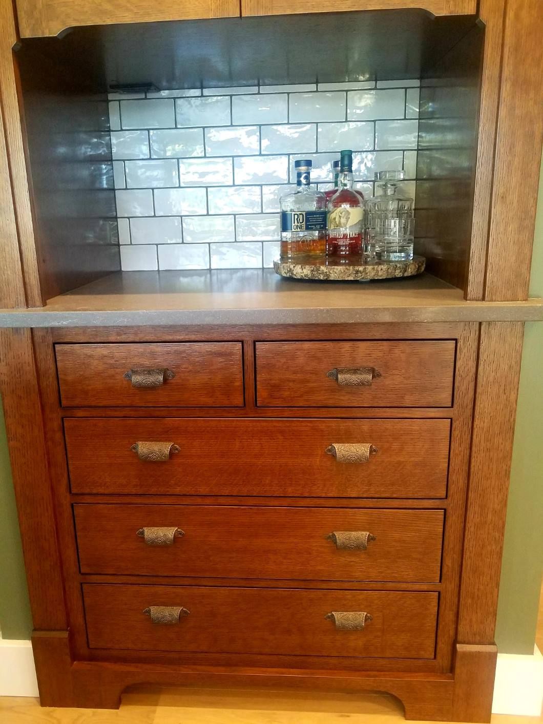 A wooden hutch with drawers and a subway-tile backsplash, featuring a countertop holding several glass liquor bottles.