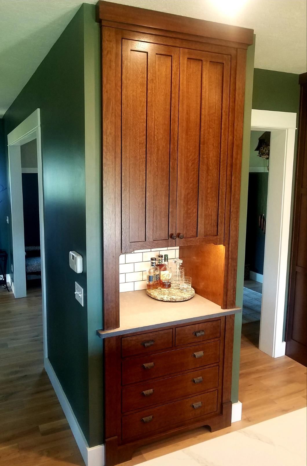 A tall wooden cabinet with drawers, a counter, and upper cupboards built into a corner with dark green walls.