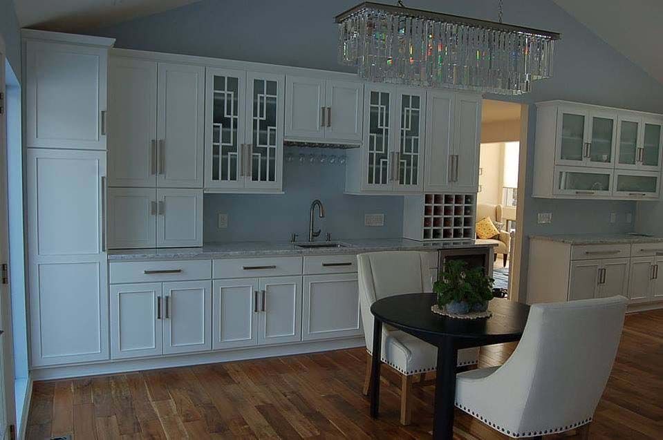 A kitchen with white cabinets, wood flooring, and a dining table with two white chairs beneath a crystal chandelier.