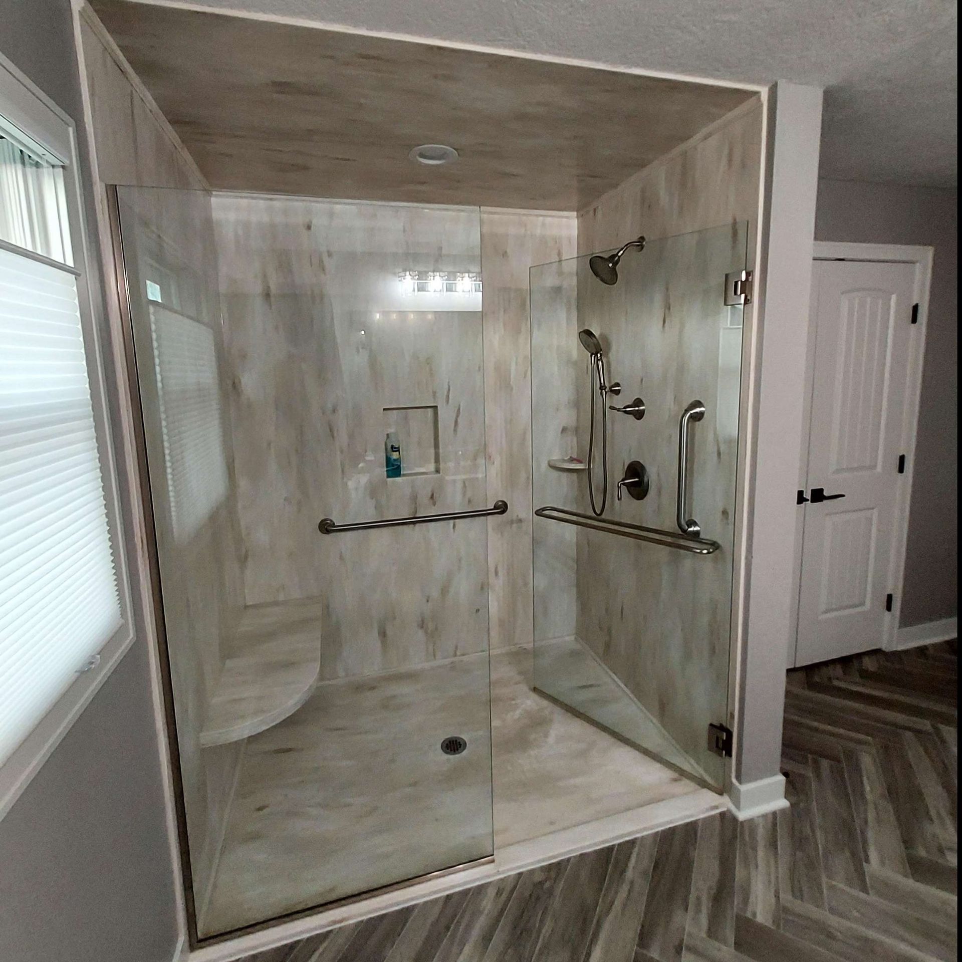 A walk-in shower with light wood-patterned tile, glass doors, a built-in bench, and chrome grab bars and fixtures.
