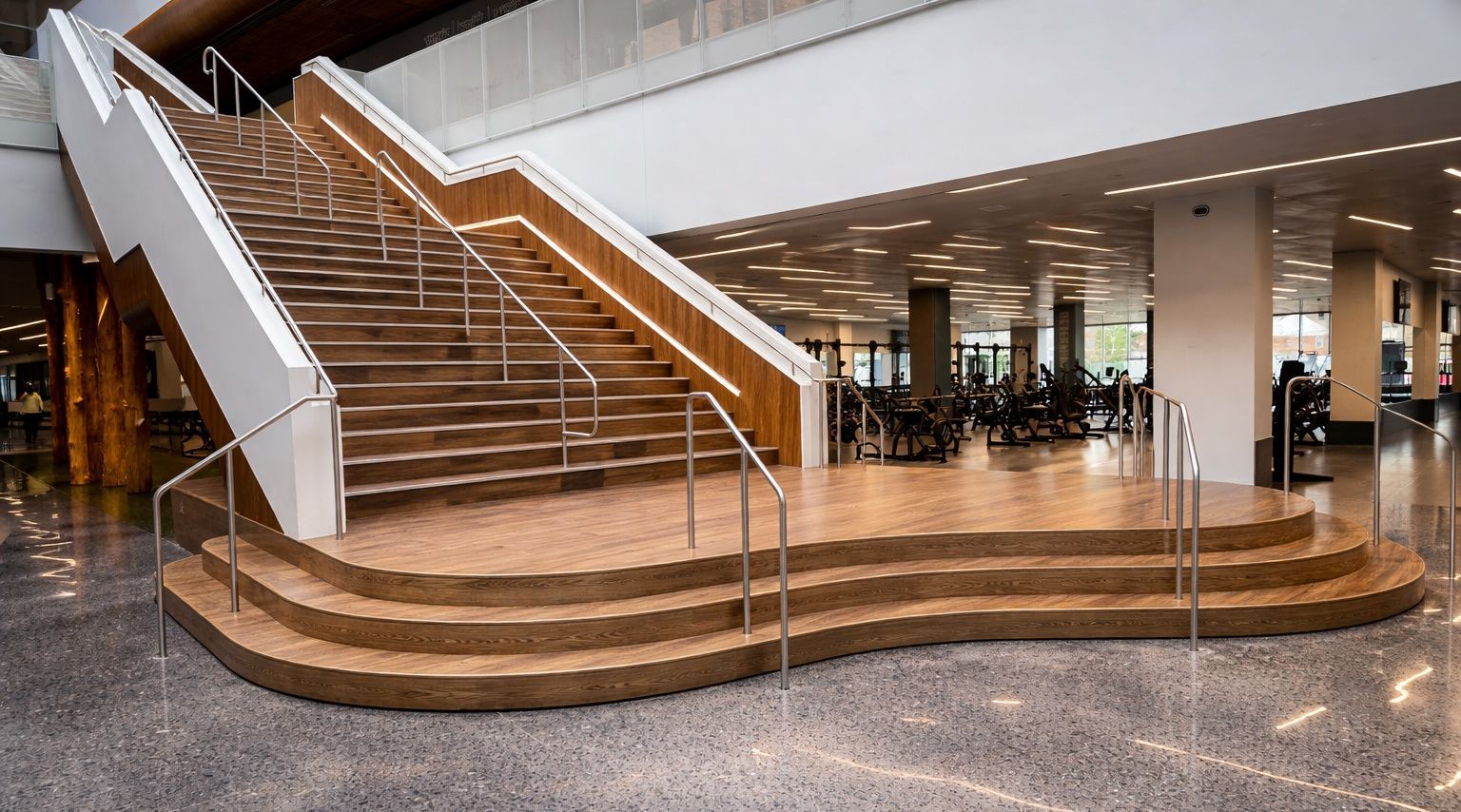 Wide-angle shot of a grand wooden staircase with curved steps in a bright, modern building lobby with marble floors.