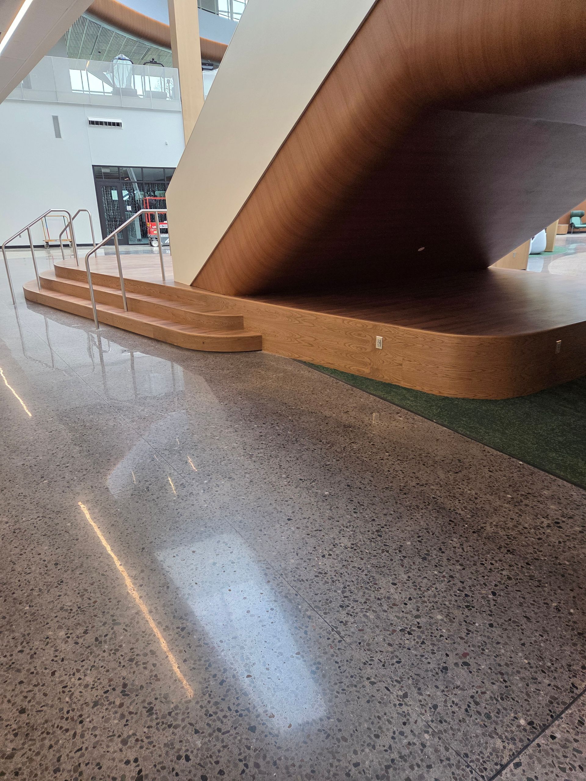 A staircase with wooden steps and a railing, featuring a large, overhanging wooden structure in a polished lobby.