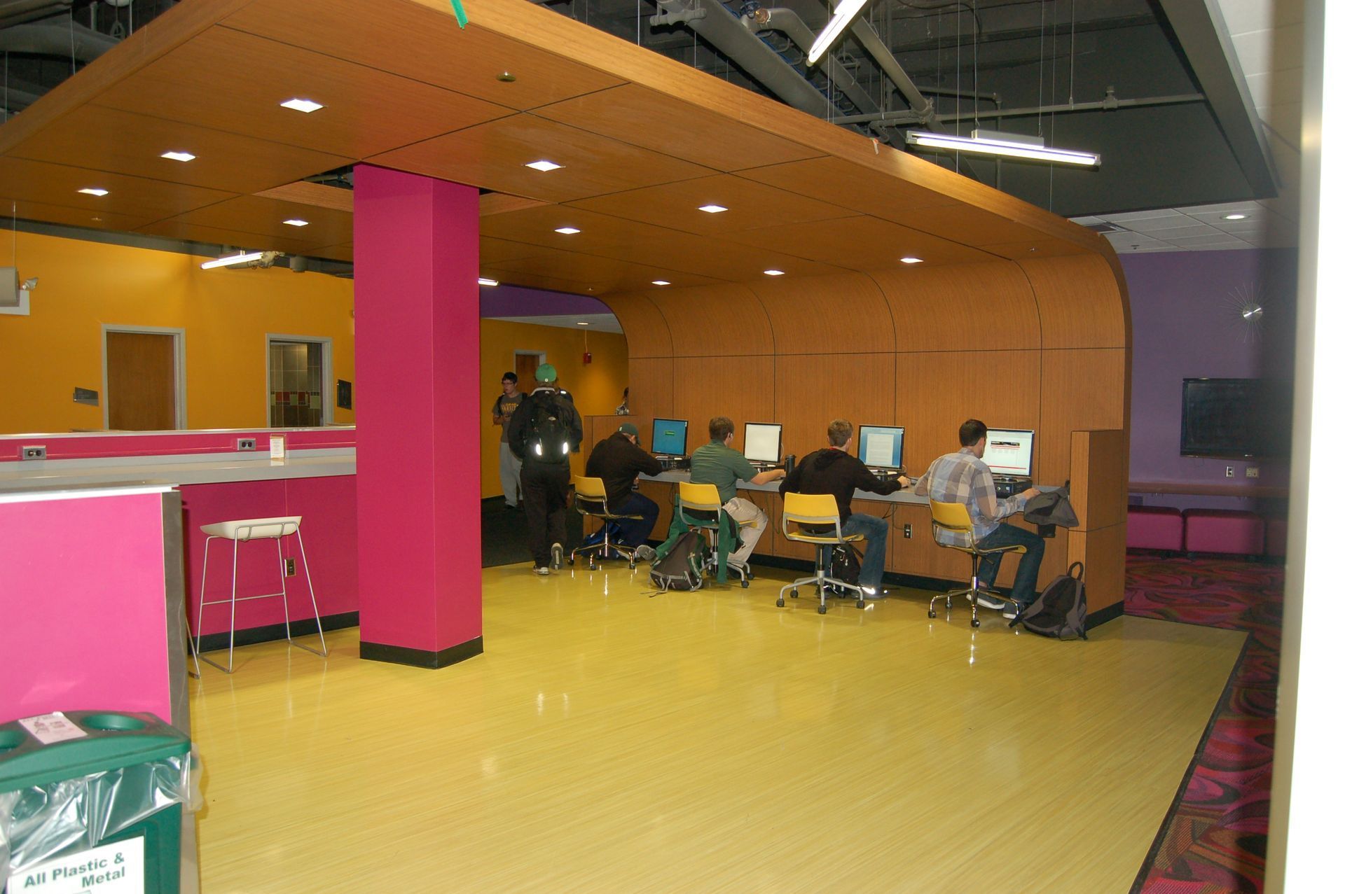 A computer station area with students working at desks under a curved wooden ceiling, set in a colorful room.
