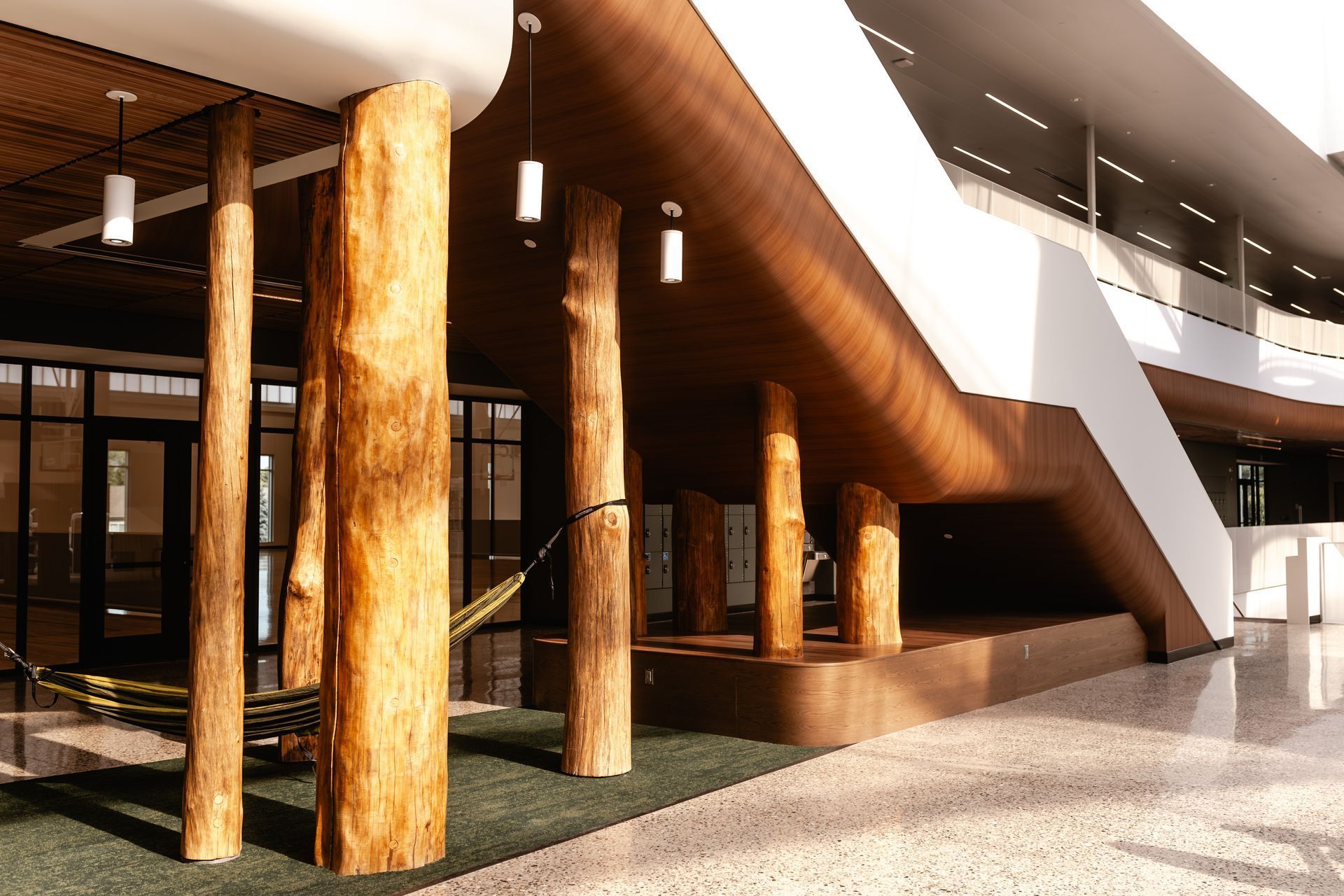 Modern lobby with large wooden columns, glass walls, and polished floors.