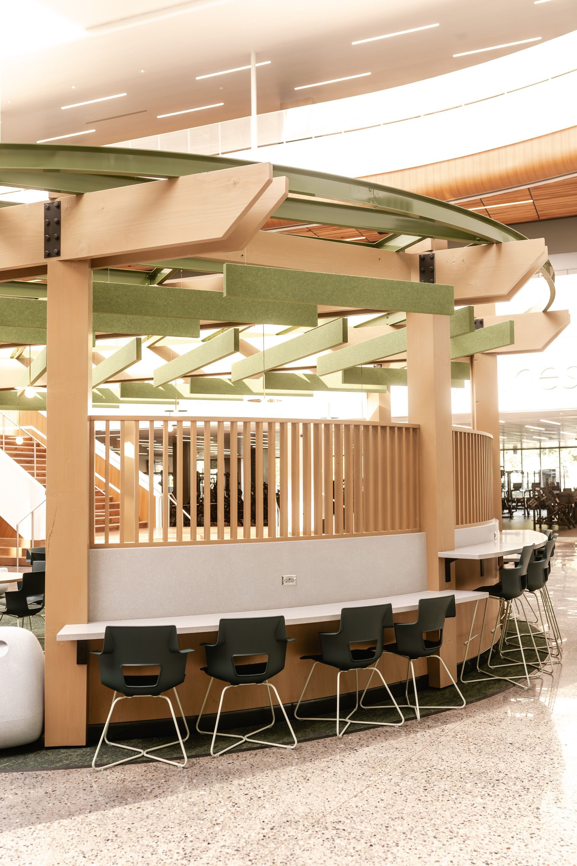 Curved café seating area with wooden paneling, green chairs, and a decorative ceiling in a modern interior