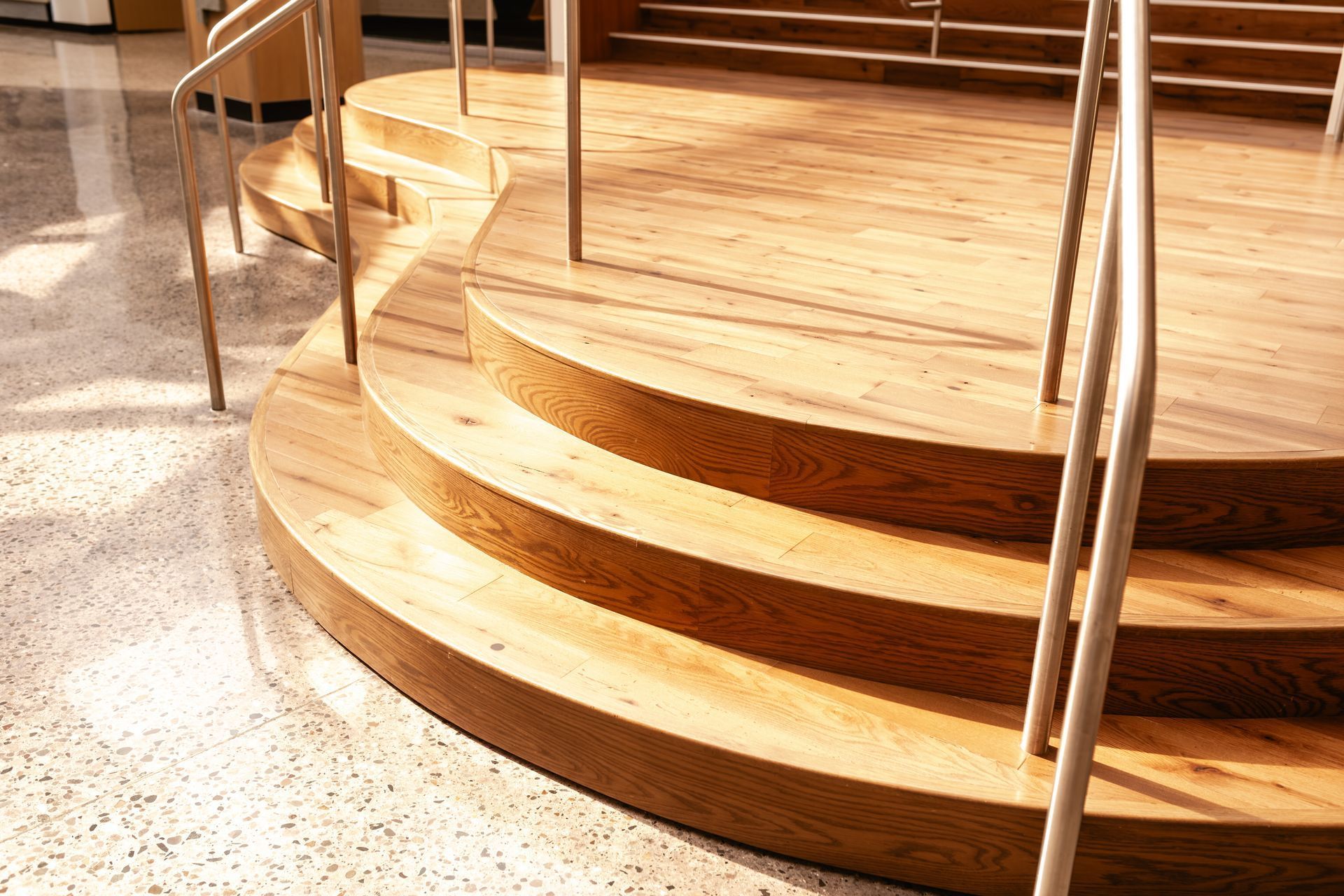 Curved wooden staircase with metal railings on a speckled floor, lit by warm indoor light