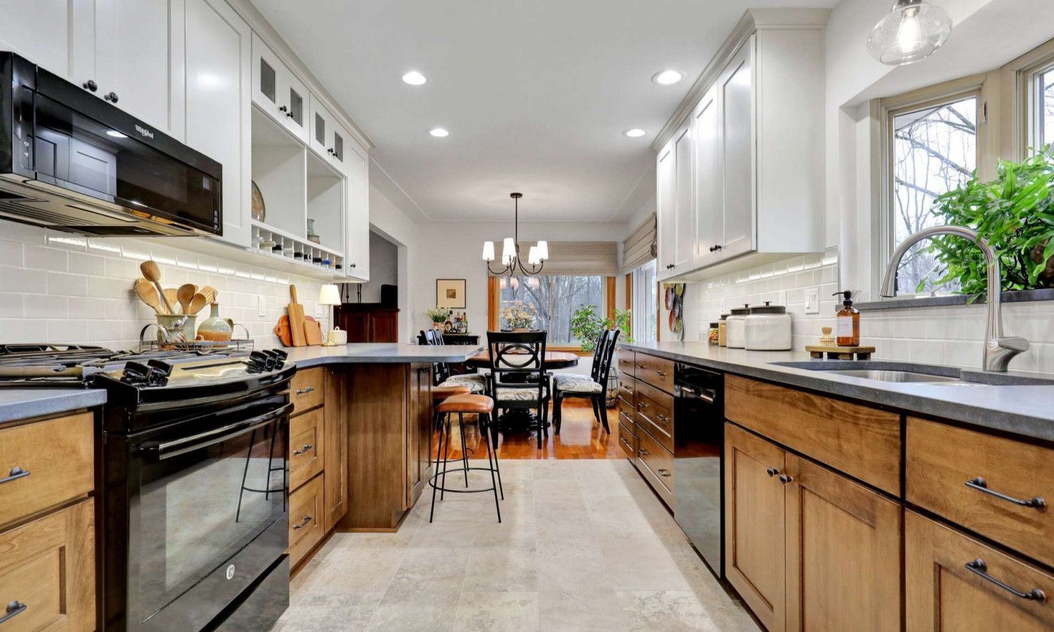 A modern kitchen featuring white upper cabinets, wood lower cabinets, black appliances, and a breakfast bar with stools.