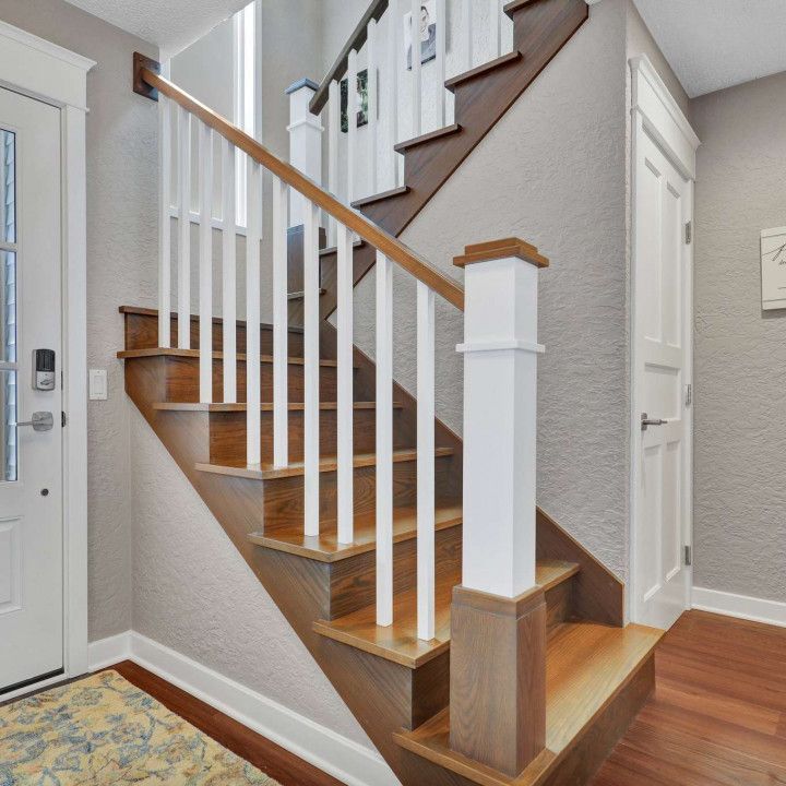 A wooden staircase with white spindles and railings ascends next to a white door in a neutral-toned residential entryway.