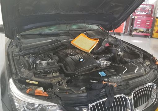 Car with open hood, engine visible, air filter removed and placed on top.