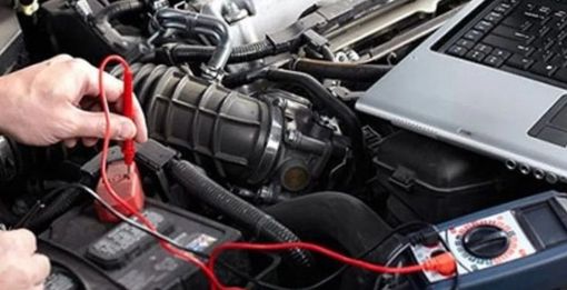 Person using a multimeter to diagnose a car engine, laptop nearby.