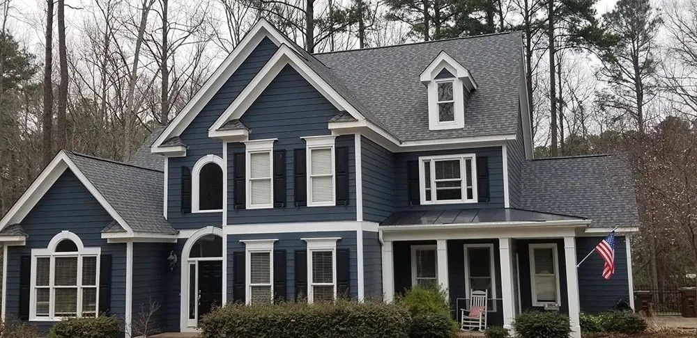 Two-story blue house with white trim and black shutters, American flag.