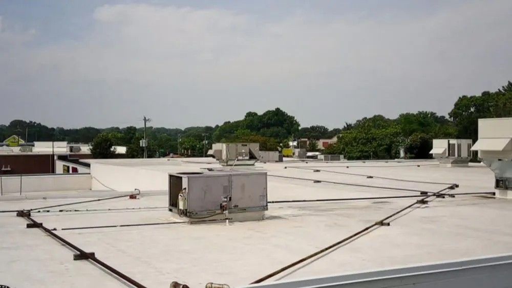 A flat white roof with HVAC units, cabling, and trees in the background under a cloudy sky.