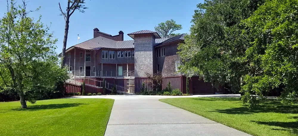 Large home with a long driveway and surrounding greenery on a sunny day.