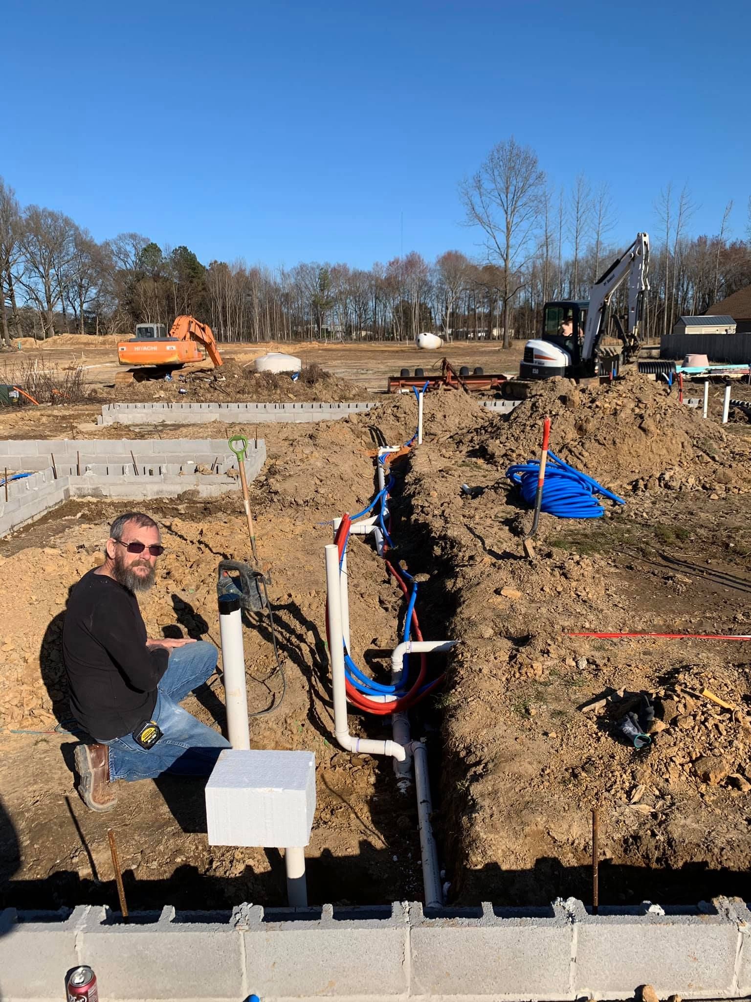 A man is sitting on a pipe in the dirt at a construction site.
