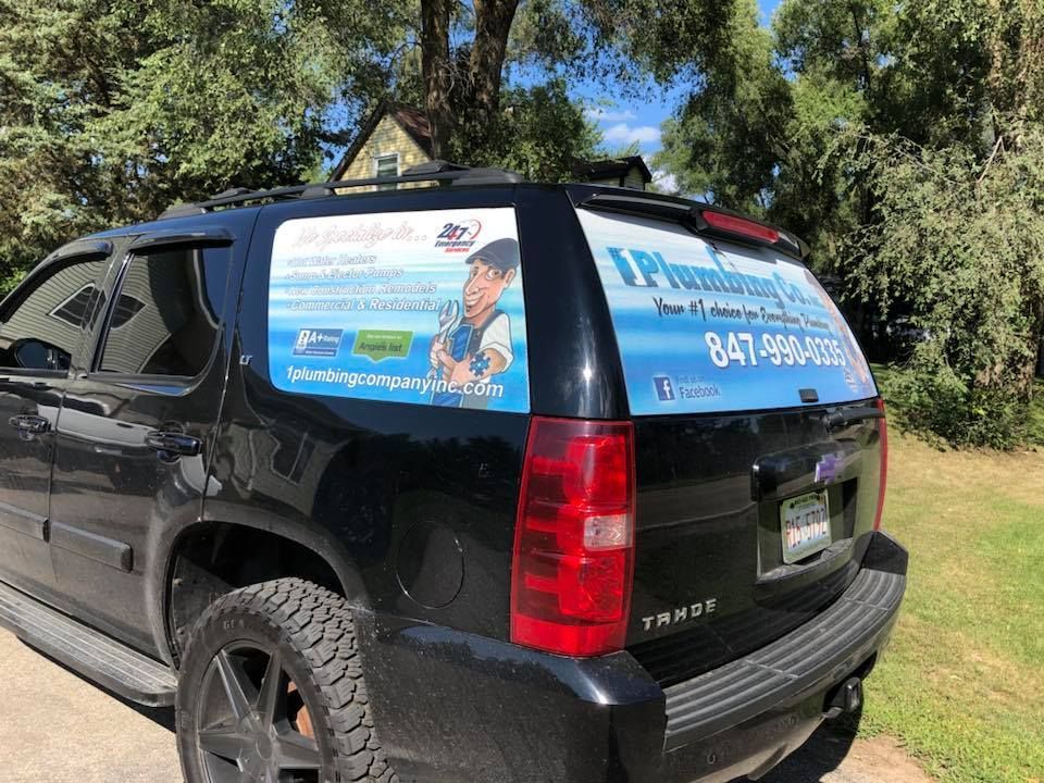 A black suv with a plumber on the back window is parked in a driveway.
