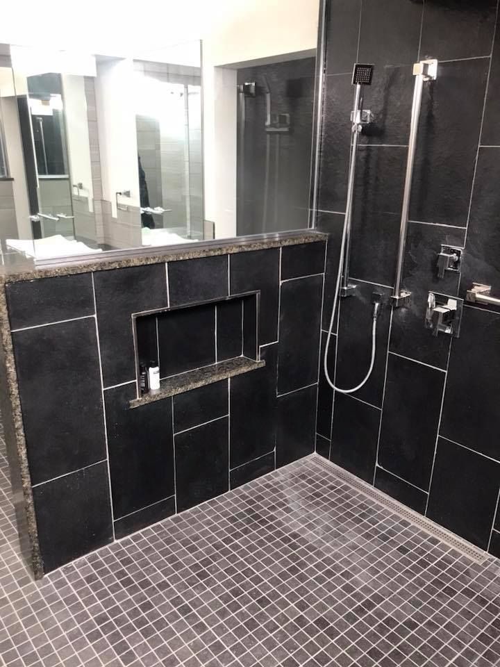 A bathroom with black tiles and a walk in shower.