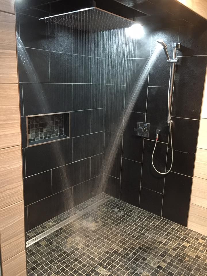 A shower with black tiles and a stainless steel shower head.