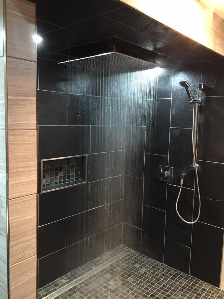 A shower with black tiles and a large shower head.