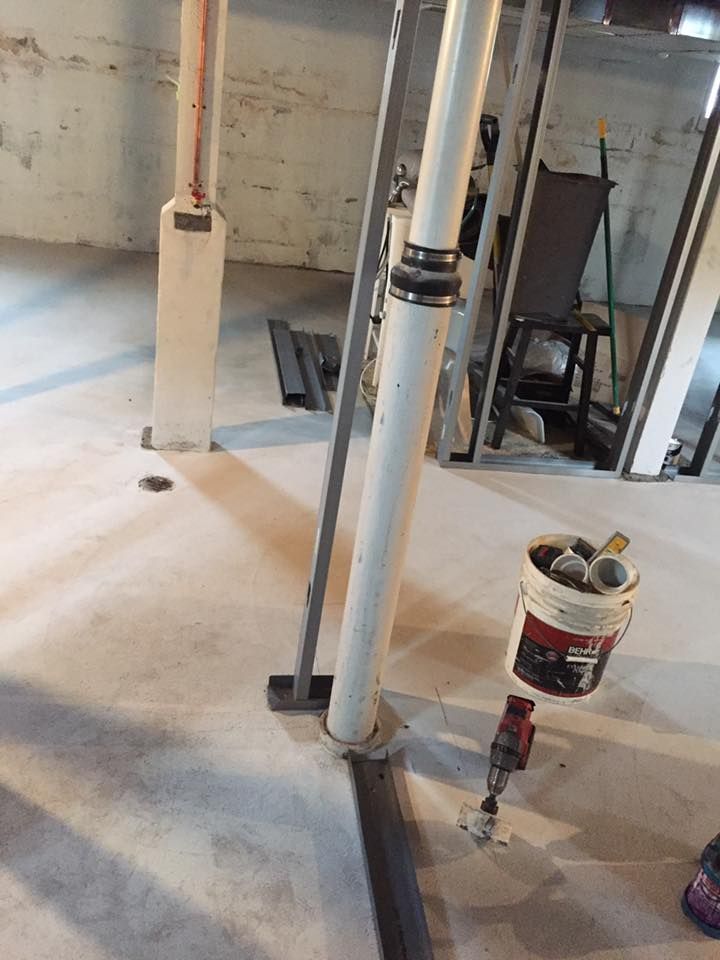 A bucket of paint is sitting next to a pipe in a basement.