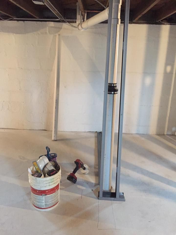 An empty basement with a bucket of tools on the floor.