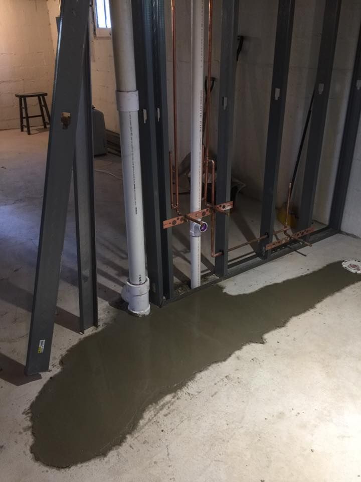 A basement with a lot of pipes and concrete on the floor.