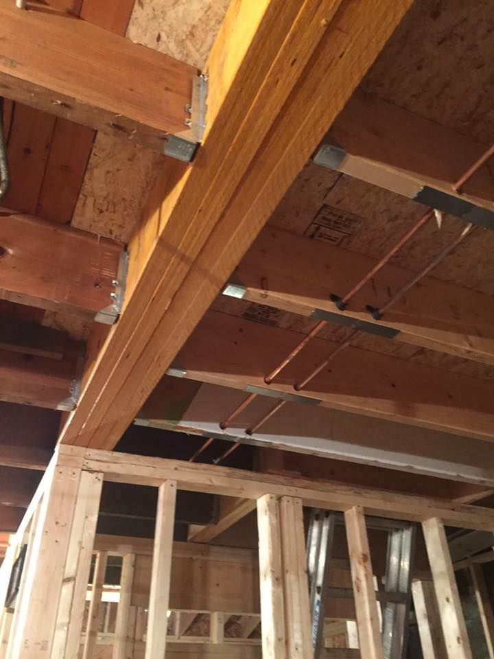 A house is being built with wooden beams and pipes coming out of the ceiling.