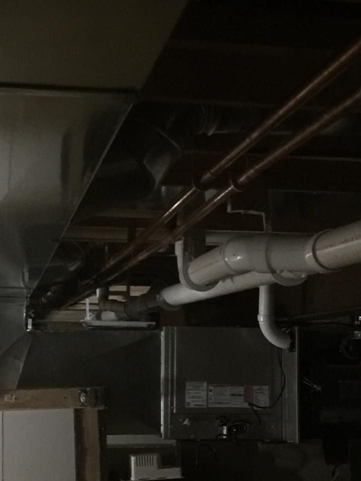 A bunch of pipes are hanging from the ceiling of a basement.