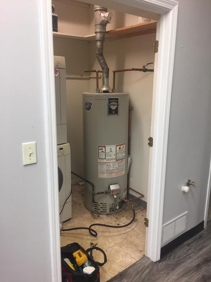 A water heater is sitting in a laundry room next to a washer and dryer.