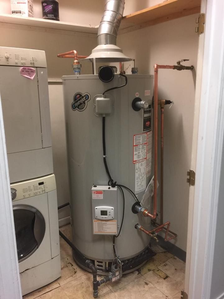 A water heater is sitting in a laundry room next to a washer and dryer.