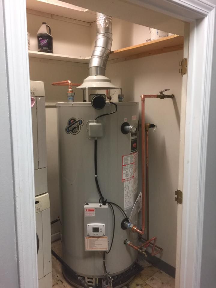 A water heater is sitting in a laundry room next to a washer and dryer.