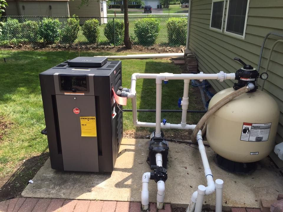 A pool heater is sitting next to a sand filter on the side of a house.