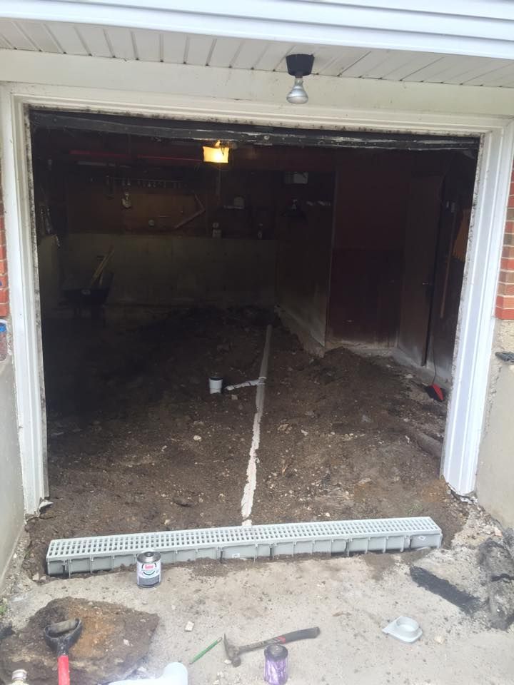 A garage door is being opened and a drain is being installed.
