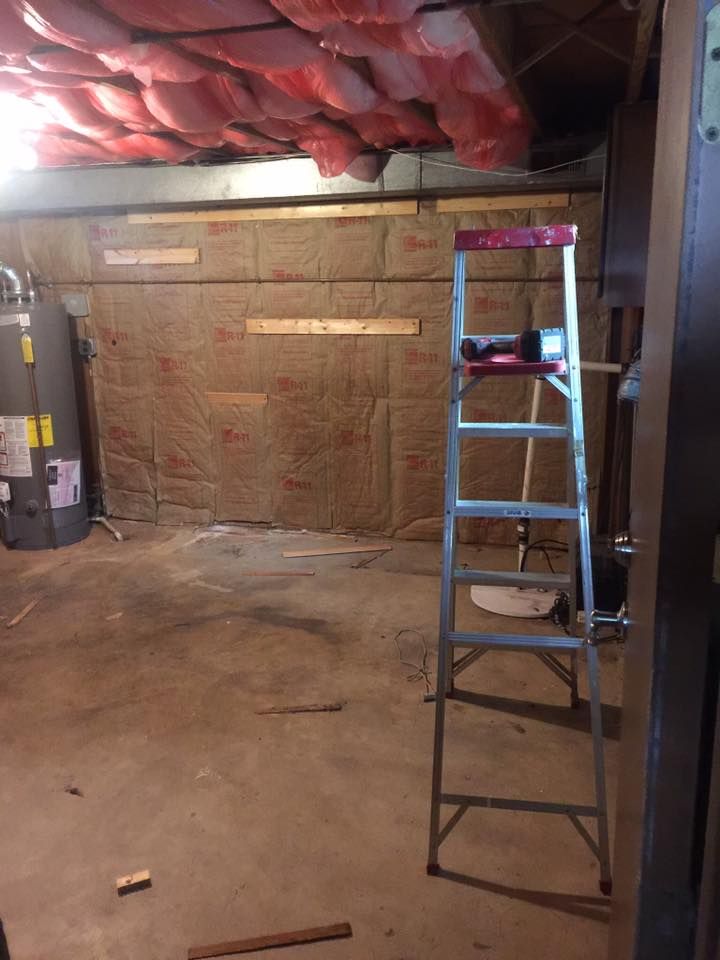A ladder is sitting in a basement next to a water heater.