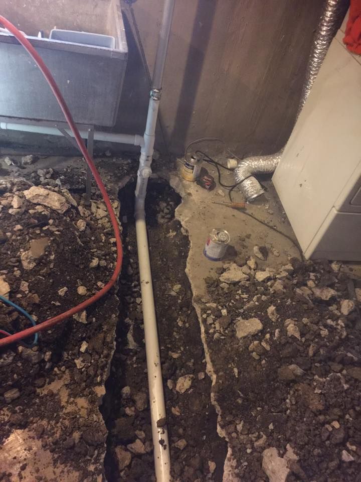 A pipe is laying in the dirt in a basement next to a furnace.