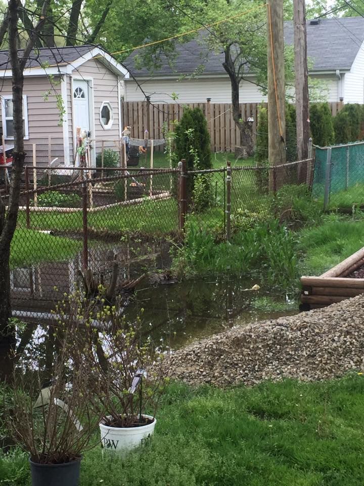 A flooded yard with a fence and a house in the background.