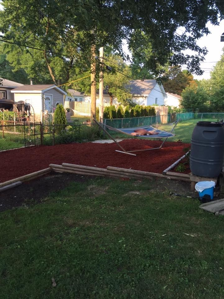 A large black barrel is sitting in the middle of a lush green yard.