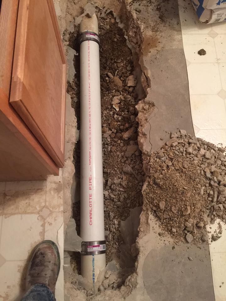 A person is standing next to a white pipe in the dirt.