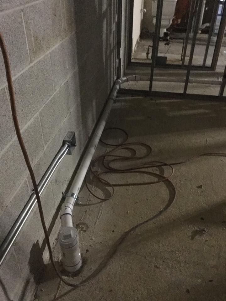 A snake is laying on the floor next to a pipe in a basement.
