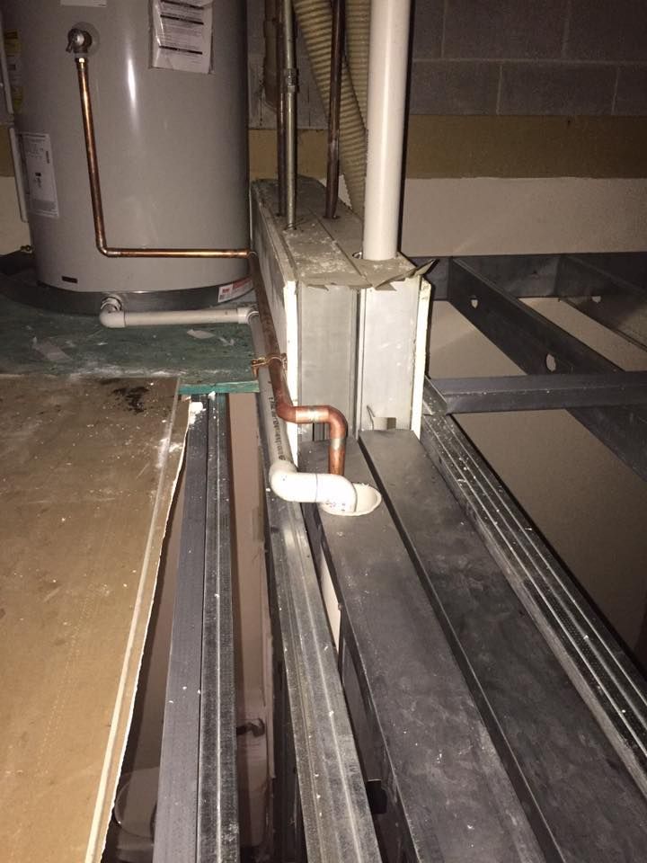 A water heater is sitting next to a window in a basement.