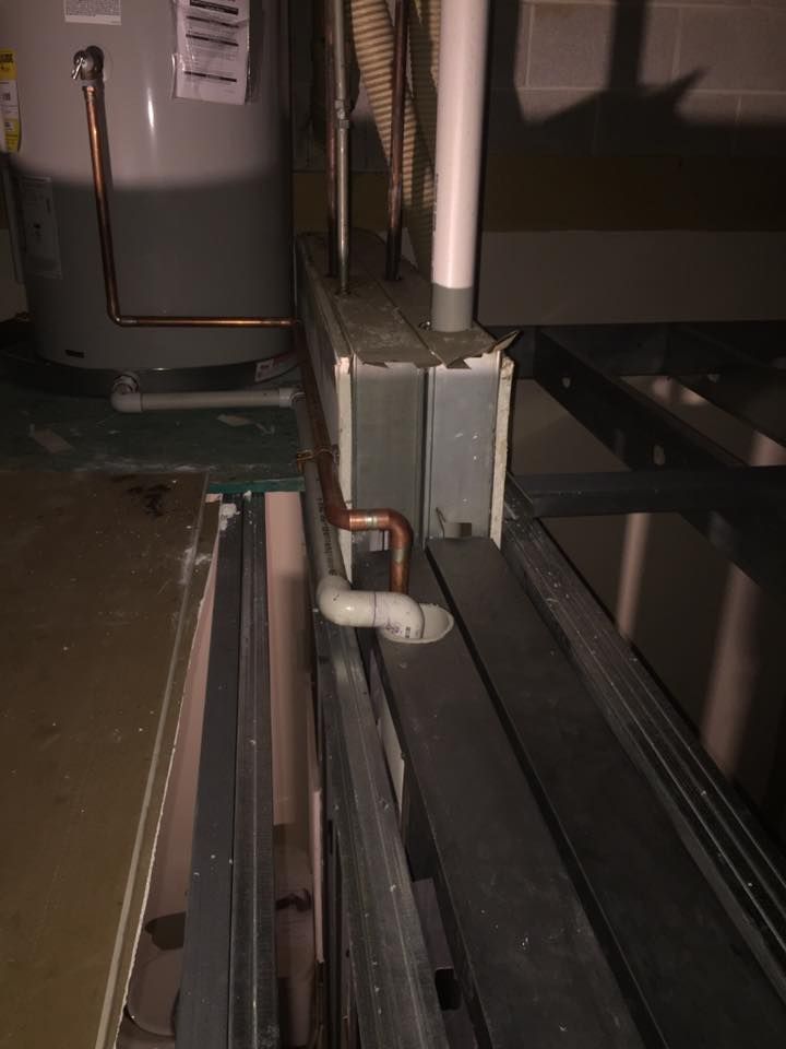 A water heater is sitting next to a pipe in a basement.