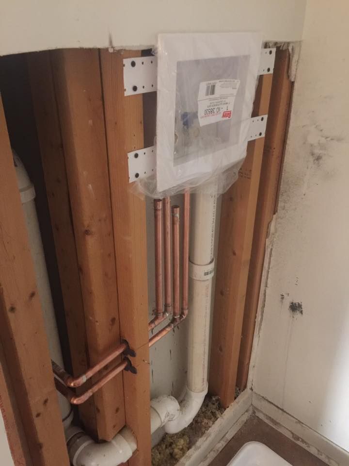 A bathroom with a toilet , sink , and copper pipes.