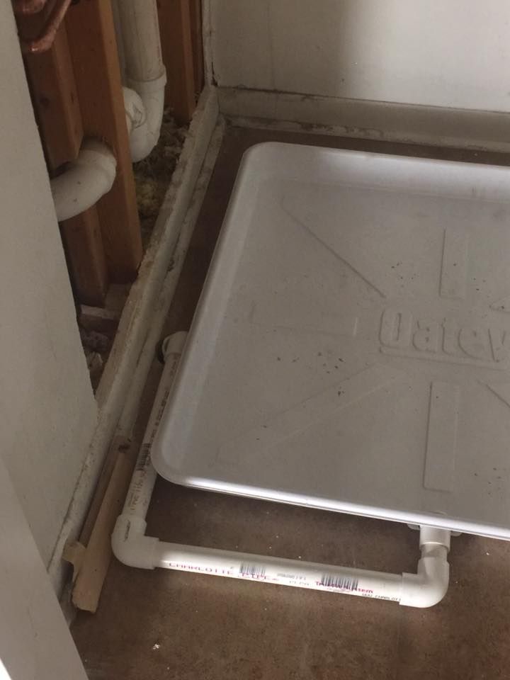 A white tray is sitting on the floor next to a pipe.