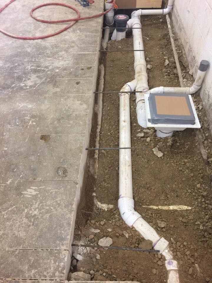 A bunch of pipes are laying in the dirt next to a wall.