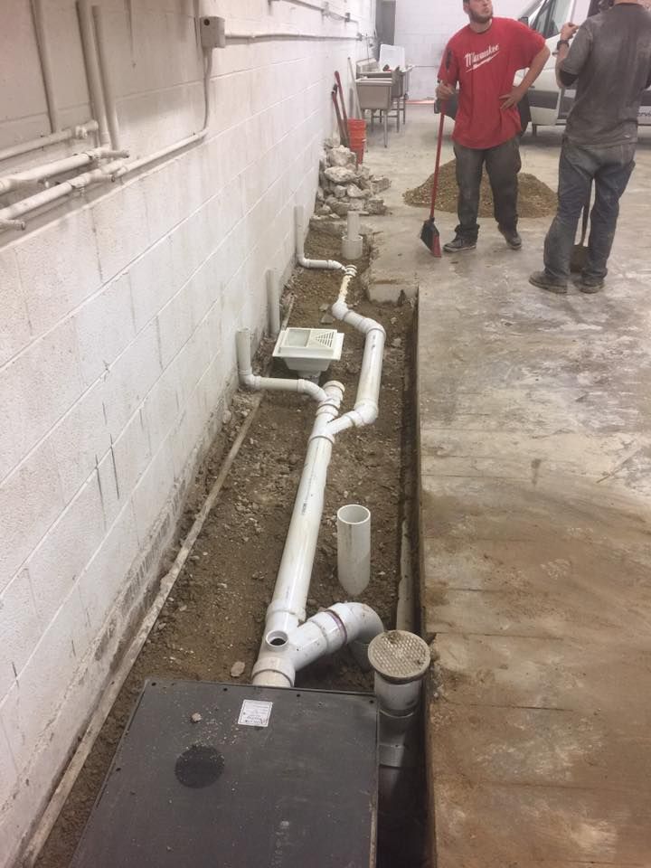 A group of men are working on a drainage system in a basement.