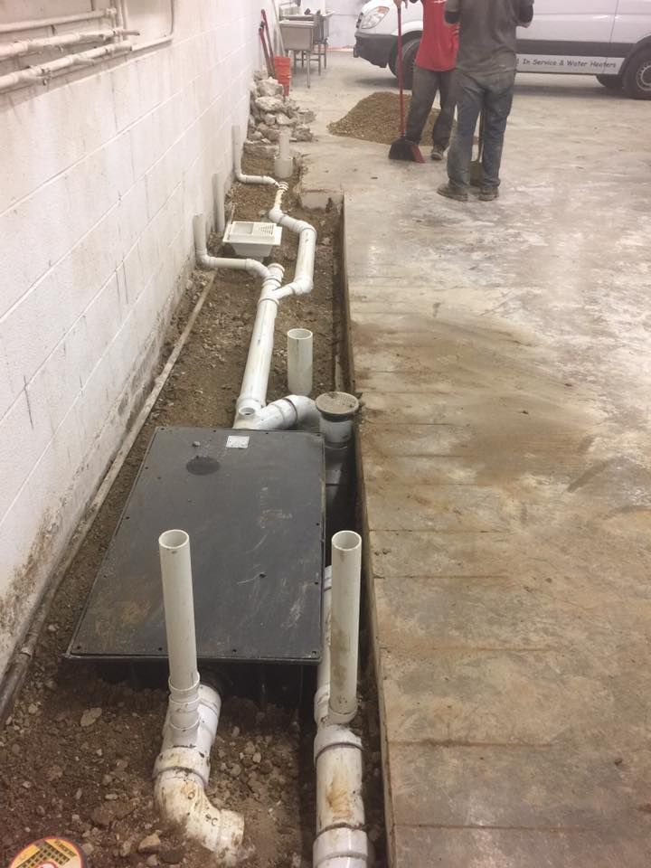 A group of men are working on a drainage system in a garage.