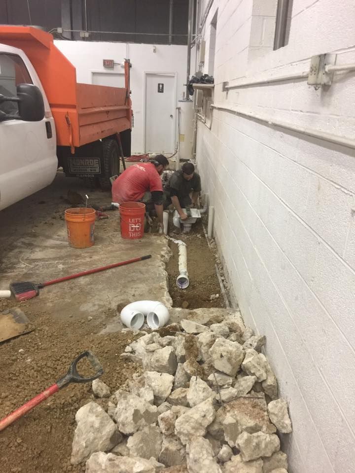 A man is working on a pipe in a garage next to a dump truck.